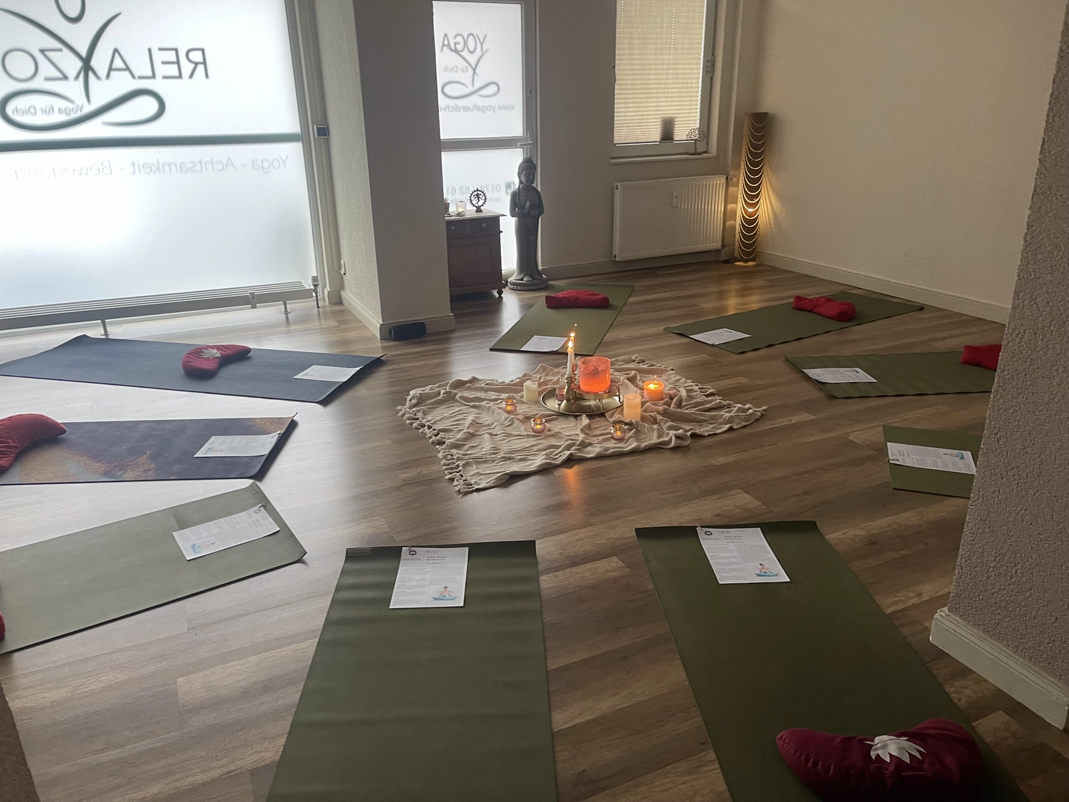 Yoga für Dich - Yoga Kurse - Ein ruhiges Yoga- oder Meditationsstudio mit mehreren Matten, die kreisförmig um einen kerzenbeleuchteten Mittelpunkt angeordnet sind.